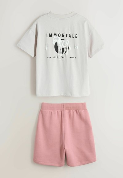 Hvid kortærmet t-shirt med zebragrafik og teksten "IMMORTALE", kombineret med lyserøde shorts med elastik i taljen, lagt fladt på en hvid baggrund.