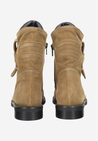 Para beżowych zamszowych botków za kostkę z czarnymi podeszwami, bocznymi zamkami i dekoracyjnymi przeszytymi paskami z tyłu na białym tle.