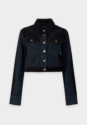Femme aux cheveux clairs portant une veste en jean bicolore noire et bleu foncé avec un jean assorti et des bottes noires à talons.