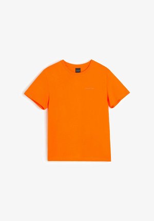 Jasno pomarańczowy T-shirt z krótkim rękawem i okrągłym dekoltem, z małym białym logo marki na lewej piersi na białym tle.