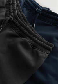 Zwei Paar Jogginghosen, eine schwarz und eine marineblau, mit einem gerippten Elastikbund und verstellbaren Kordeln sowie einer glatten Stofftextur.