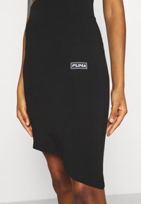 Svart jerseykjol med asymmetrisk fåll, med en vit Puma-logotyp på lappen. Mjuk struktur och figurnära design är framträdande.