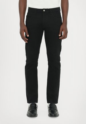 Sorte denim jeans med rett snitt, fem lommer, sølvfarget knappelukking og en jevn tekstur. Brukt med sorte loafers.