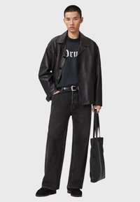 Czarna skórzana kurtka, czarny t-shirt z grafiką, szerokie czarne dżinsy i czarne buty, noszący fakturowaną czarną torbę na ramię.