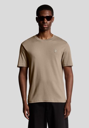 T-shirt en coton beige avec un col rond et des manches courtes, doté d'un petit logo brodé sur la poitrine et d'une texture lisse.
