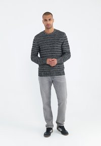 Grau gestreifter Strickpullover mit Rundhalsausschnitt, getragen mit hellgrauen Jeans und schwarzen Sneakers mit weißen Akzenten.