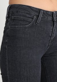 Jeans de mezclilla de lavado oscuro con un diseño ajustado, que cuentan con una cintura de altura media, costuras visibles y colocación estándar de los bolsillos.