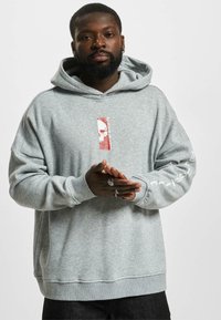 Felpa grigia oversize con cappuccio regolabile. Presenta una grafica di un teschio in rosso e bianco sul davanti e testo stampato lungo la manica.