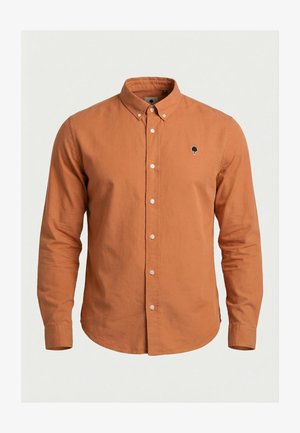 Camisa de manga larga color óxido con botones y cuello abotonado, con un pequeño logo bordado en negro de un árbol en el pecho izquierdo.