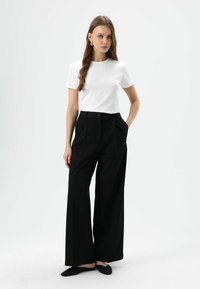 Witte top met korte mouwen, gecombineerd met hoge taille zwarte wijde broek. De broek heeft voorzakken en een sluiting met een enkele knoop.