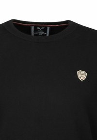 Schwarzer Strickpullover mit Rundhalsausschnitt, ausgestattet mit einem kleinen gestickten Emblem auf der linken Brust. Strukturierter Stoff und taillierte Passform.