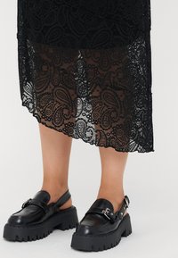 Čierna čipkovaná sukňa s paisley vzorom a zúženým lemom, kombinovaná s čiernymi koženými slingback topánkami s robustnou podrážkou a detailom na pracke.
