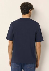 Námořnická modrá polokošile s krátkým rukávem a klasickým kulatým výstřihem. Měkká tkanina, volný střih a jednoduchý design, zobrazený z pohledu zezadu.