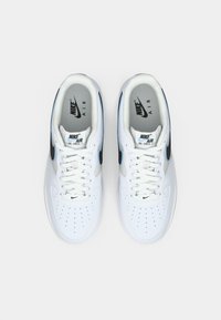 Nike Air Force 1 Sneaker aus weißem Leder mit schwarzen Akzenten. Merkmale sind eine perforierte Zehenpartie, flache weiße Schnürsenkel und eine gepolsterte Sohle.