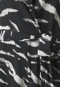 Tissu à motifs noir et blanc avec une finition texturée, présentant un détail de ceinture nouée et un design enroulé qui met en valeur la taille.