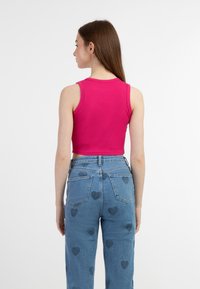 Top corto rosa a costine, aderente, con ampie aperture per le braccia, abbinato a jeans blu a vita alta con motivo a cuore. Texture liscia, design casual.