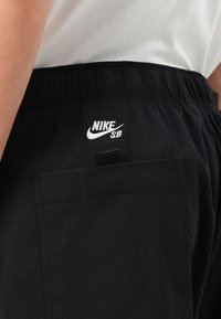 Black athletic shorts with elastic waistband, featuring a white Nike SB logo, a flat pocket on the back, and a smooth, lightweight fabric texture.