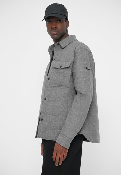 Harmaa pehmustettu takki nappikiinnityksellä, kahdella rintataskulla ja kauluksella. Yhdistetty mustaan lippikseen ja mustiin housuihin. Pehmeä rakenne, muotoiltu istuvuus.