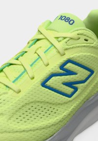 Ανδρικό αθλητικό παπούτσι σε λαμπερό κίτρινο λουράκι με μπλε λεπτομέρειες, διαθέτει μαξιλαρωμένη γλώσσα, κλείσιμο με κορδόνια και λογότυπο "N" στο πλάι.