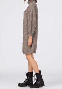 Ljusbrun virkadräkt med hög hals och ballongsärmar, matchad med svarta snörade anklabels med spänne.