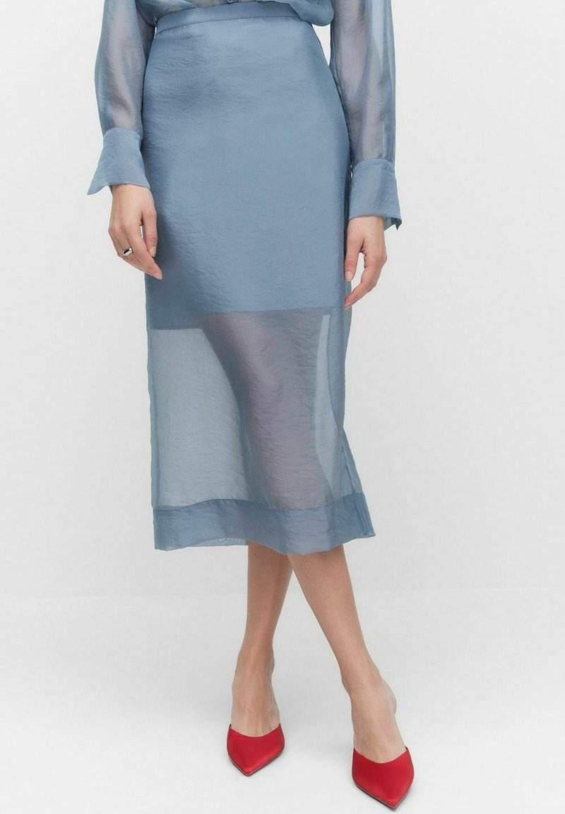 Ljusblå, genomskinlig midikjol med en fast nederkant. Mjuk textur med en åtsittande midja, tillsammans med röda pumps med spetsig tå.