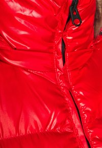 Gros plan d'une veste matelassée rouge brillante avec une fermeture éclair noire partiellement ouverte.