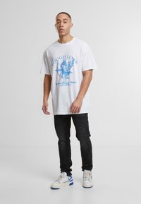 Valge lühikeste varrukatega T-särk, millel on sinine graafiline print cherubist koos tekstiga "Tough Love". Mustad teksad, millel on värvilised värvitäpid. Valged spordijalatsid.