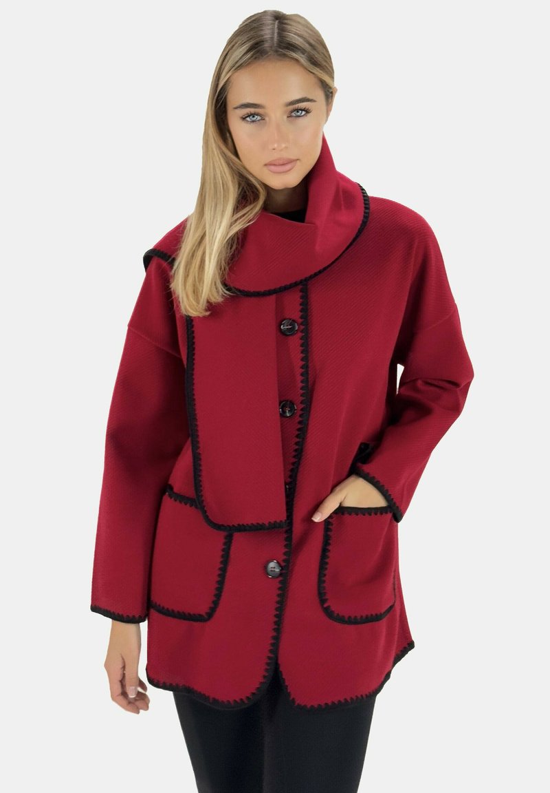 Chaqueta roja de gran tamaño con un alto cuello, botones dobles, ribete negro y grandes bolsillos. Tela texturizada con una forma estructurada.