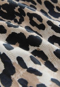 Tessuto con stampa leopardata che mostra audaci macchie nere su uno sfondo beige, realizzato in materiale morbido e textured con dimensioni del motivo variabili.