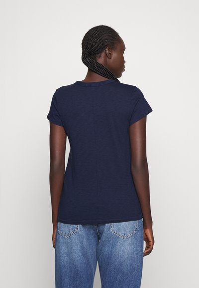 Navy blue short-sleeve T-shirt with a round neckline and a textured finish, paired with light blue denim jeans. Back view.