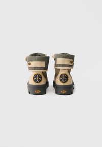 Botas em caqui e bege com colarinho acolchoado, solas de borracha e um logótipo circular com estrelas e uma bússola no salto. Detalhe com tira ajustável no tornozelo.