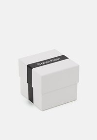 White square box with a lid, featuring a black band labeled "Calvin Klein." Smooth texture with sharp corners and minimalist design.