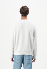Light gray sweatshirt with a crew neckline, ribbed cuffs, and hem; paired with light blue denim jeans featuring back pockets.
