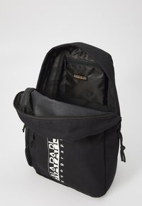 Svart ryggsäck med en zippered huvudfack, inre ficka och justerbara remmar. Har en vit varumärkeslogotyp på framsidan.