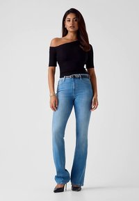 Haut noir à épaules dénudées, jean évasé bleu clair, talons hauts. Texture lisse, coupe décontractée, denim avec légère décoloration et détail ceinture.