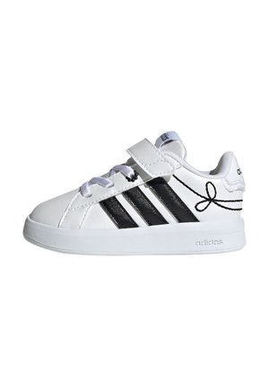 Biały sneaker Adidas z czarnymi paskami, paskiem na rzep, sznurówkami i czarną kokardką na pięcie, widziany z boku.