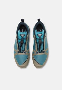 Baskets de sport bleues et grises avec un dessus texturé, un orteil renforcé et un système de laçage intégré. Semelle en caoutchouc avec des crampons de traction proéminents.