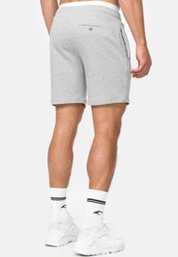 Shorts en coton gris avec une coupe décontractée, taille élastique, poches avant et une poche arrière fermée par un bouton. Texture lisse, longueur jusqu'aux genoux.