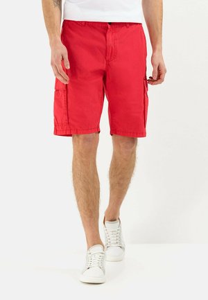 Shorts cargo rouges en tissu léger avec poches latérales, coupe au niveau du genou, et ceinture ajustable. Associés à des baskets blanches.