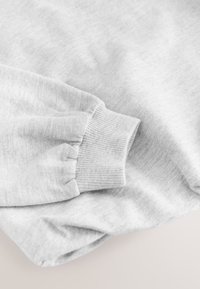 Szürke pulóver anyag bordázott mandzsettával. Puha tapintású és enyhén fényes felületű. A mandzsettán összegyűrt varrás van a szoros illeszkedés érdekében.