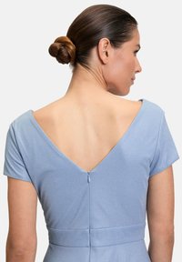 Robe bleu clair avec des manches courtes, décolleté en V au dos, tissu texturé et fermeture éclair au dos. Un léger scintillement ajoute un intérêt visuel.