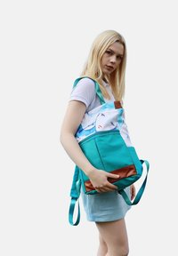 Turquoise fabric backpack with a pattern of a face in watercolor style. Features brown leather accents and adjustable straps.