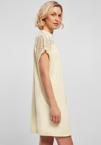 Robe jaune clair avec manches courtes ornées de dentelle. Le tissu semble doux et lisse, avec une coupe ample.
