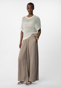 Witte lichte gebreide top met een losse pasvorm, gecombineerd met beige wijde broeken met een soepele textuur en elastische tailleband.