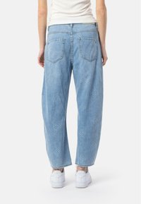 Jeans de mezclilla azul claro con un ajuste relajado, que cuentan con dos bolsillos traseros y una textura sutil y con patrón en toda la prenda. Combinados con unas zapatillas blancas.