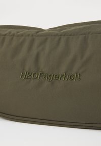 Olívazöld szövet táska texturált felülettel és hímzett "H2OFagerholt" logóval az ugyanazzal a cérnával. Puha szerkezet, minimalista design.