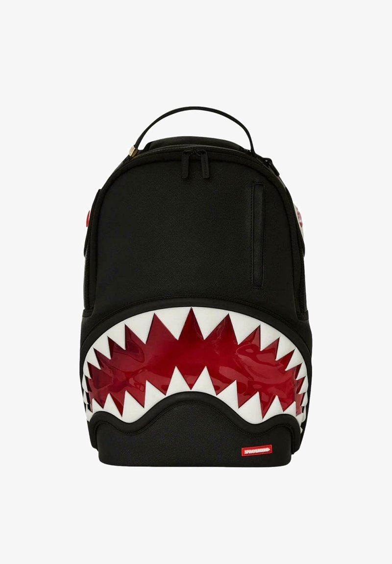 Mochila negra con diseño de boca de tiburón; presenta acentos rojos brillantes y dientes blancos. Material suave con un asa en la parte superior y cierre de cremallera.
