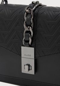 Borsa nera con motivo triangolare embossato, tracolla in catena argentata e chiusura metallica con logo del marchio. Texture liscia con design strutturato.