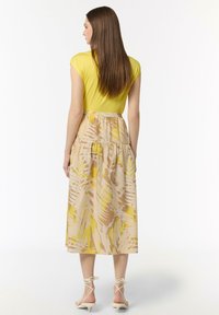 Żółta dopasowana bluzka z rękawami w kształcie półlejtka, zestawiona z lekką spódnicą o średniej długości z beżowym i żółtym wzorem liści. Beżowe sandały na paski.