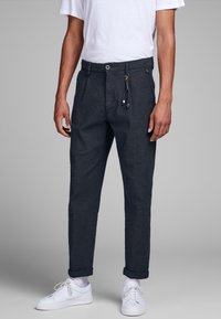 Mörka rutiga byxor med dragsko i midjan, sidofickor och uppvikta muddar, matchade med vita sneakers och en enkel vit t-shirt.